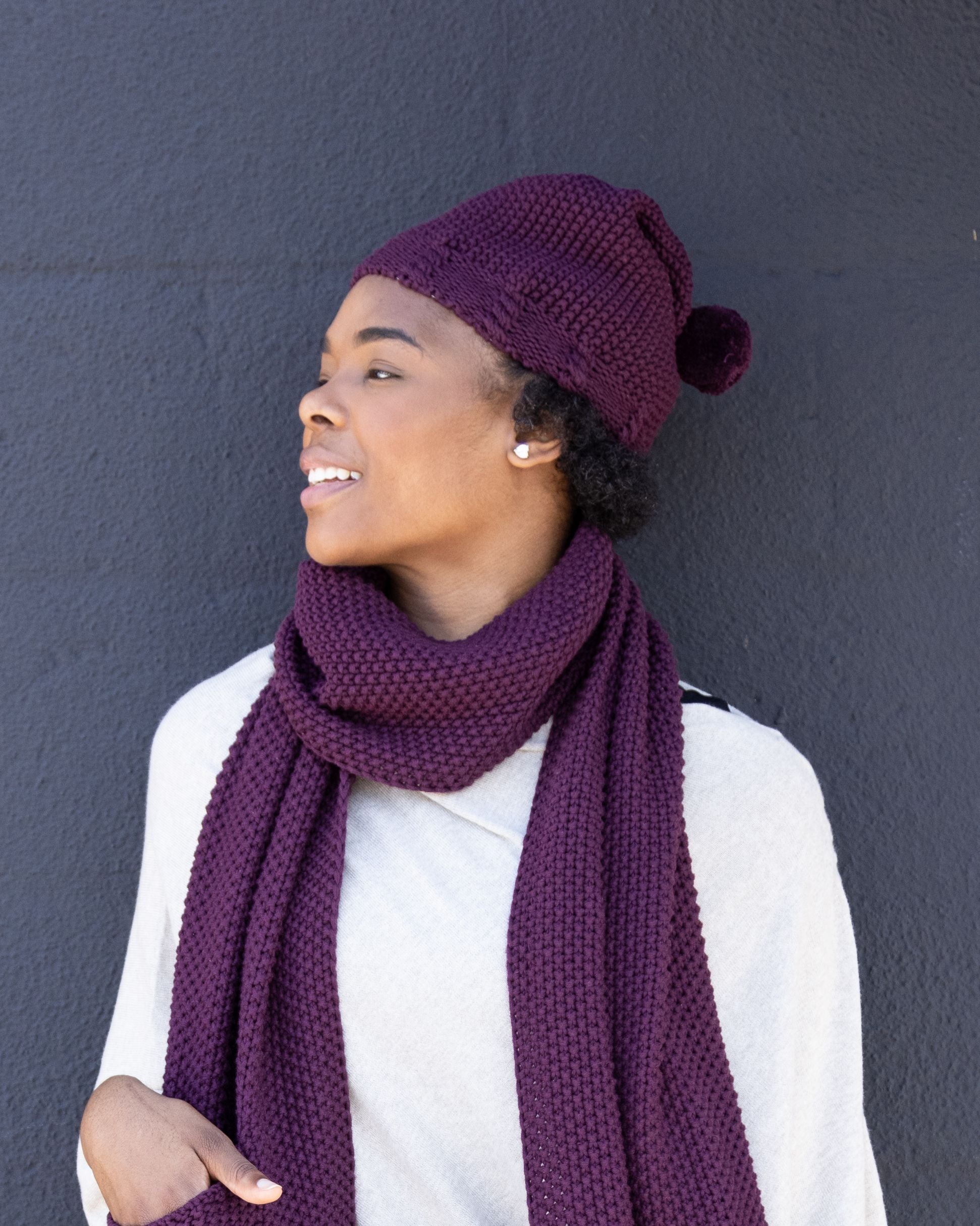 Woman wearing Organic Cotton Cozy Knit Pom Pom Hat in Mulberry which is a purple hat