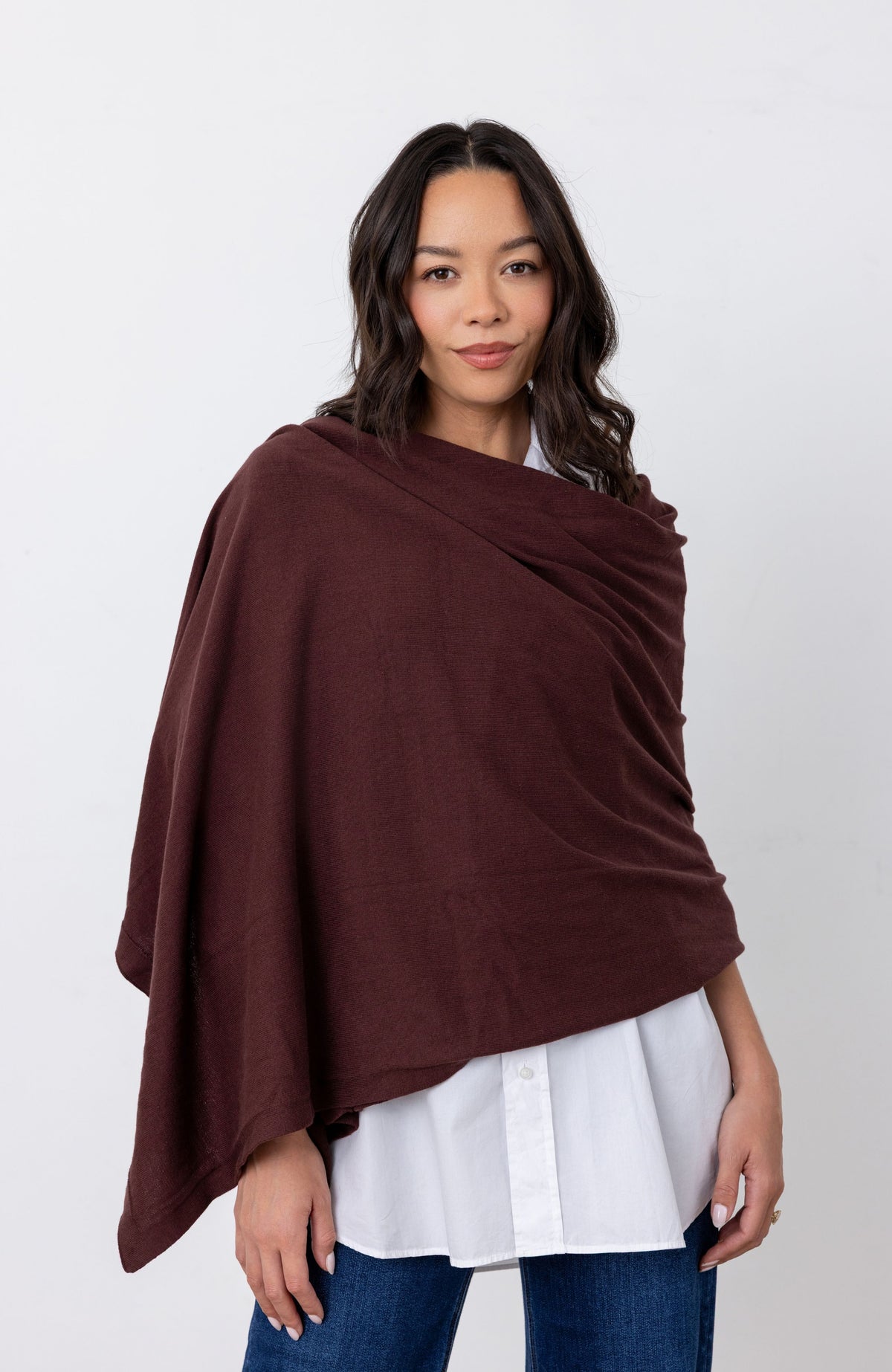 Woman wearing dark reddish-brown scarf as a shawl wrapped around her, with a white button down shirt standing against a white background