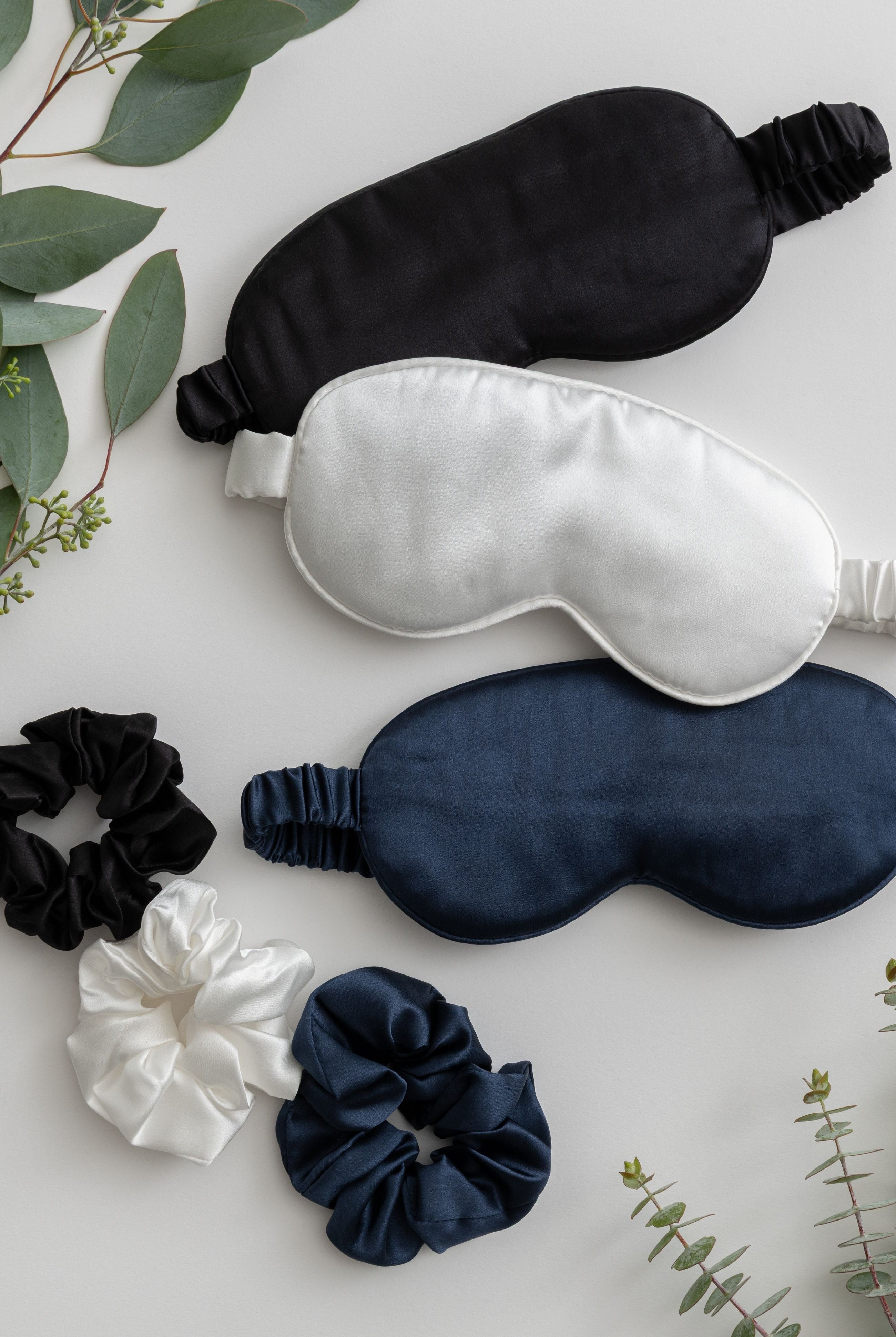 Set of black, white, and navy sleep masks with matching scrunchies on a light background.