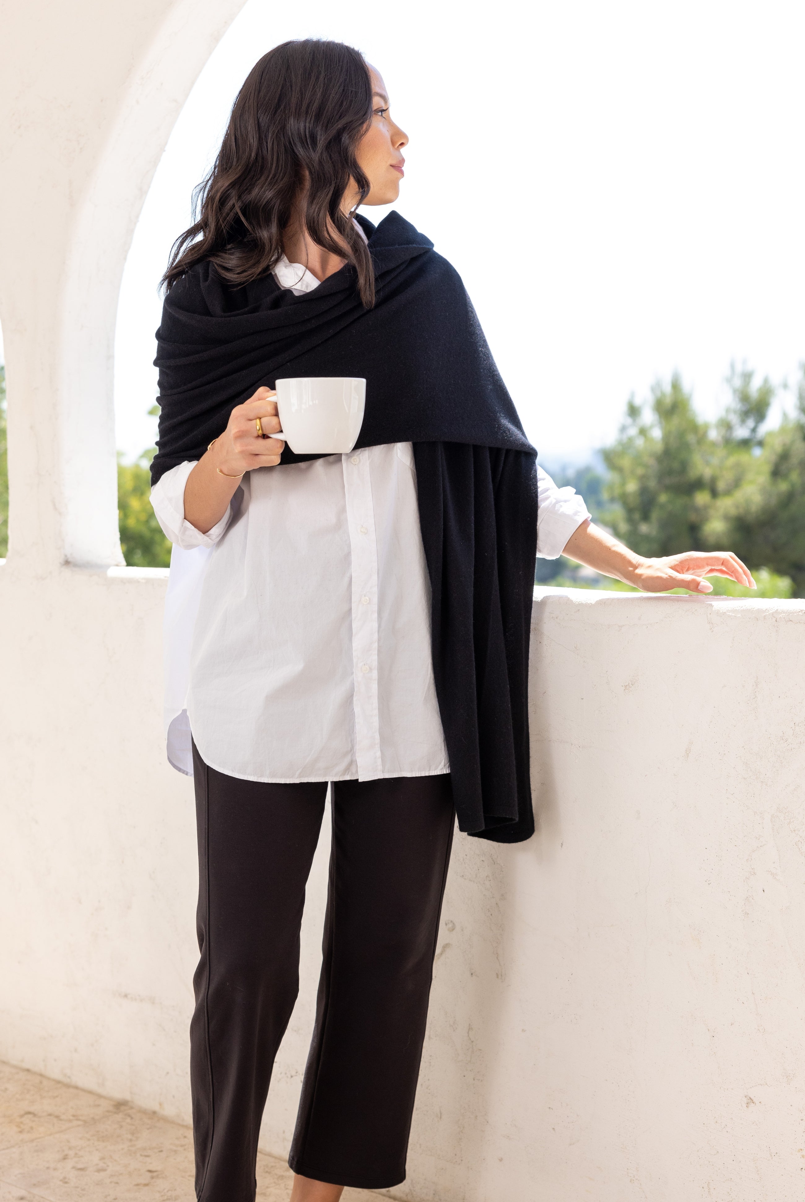 Woman shown wearing a black scarf draped around her shoulders while holding a cup of coffee