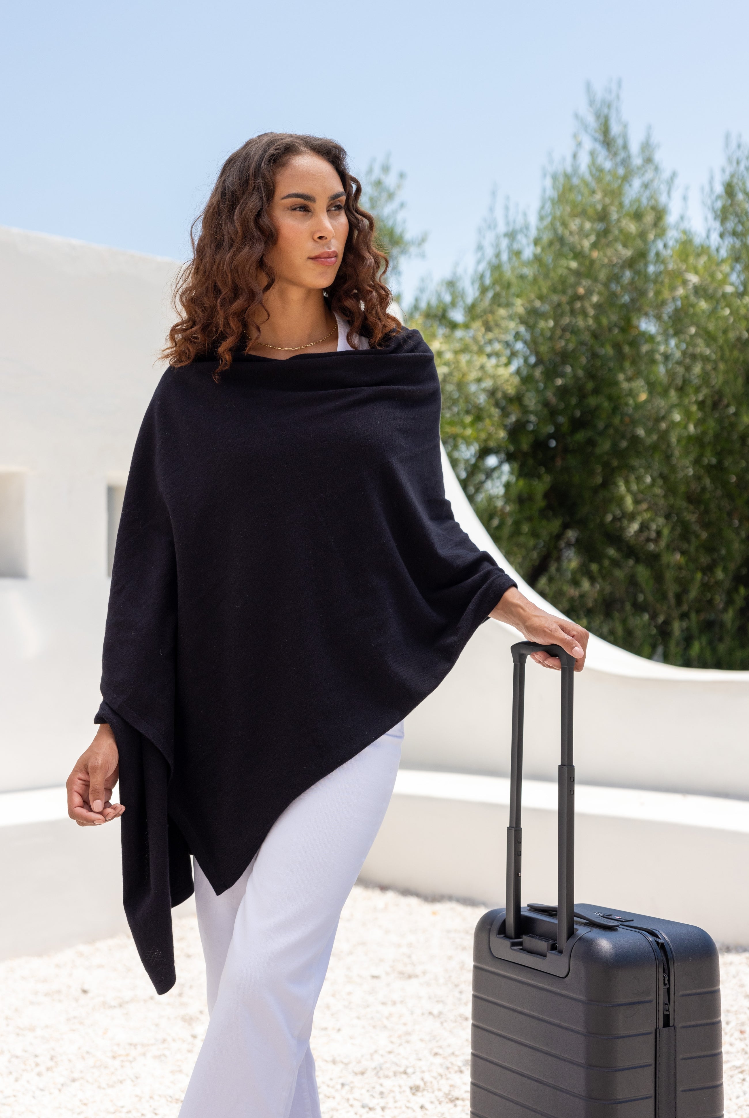 Woman shown wearing Black Scarf wrapped around shoulders with hand on suitcase handle