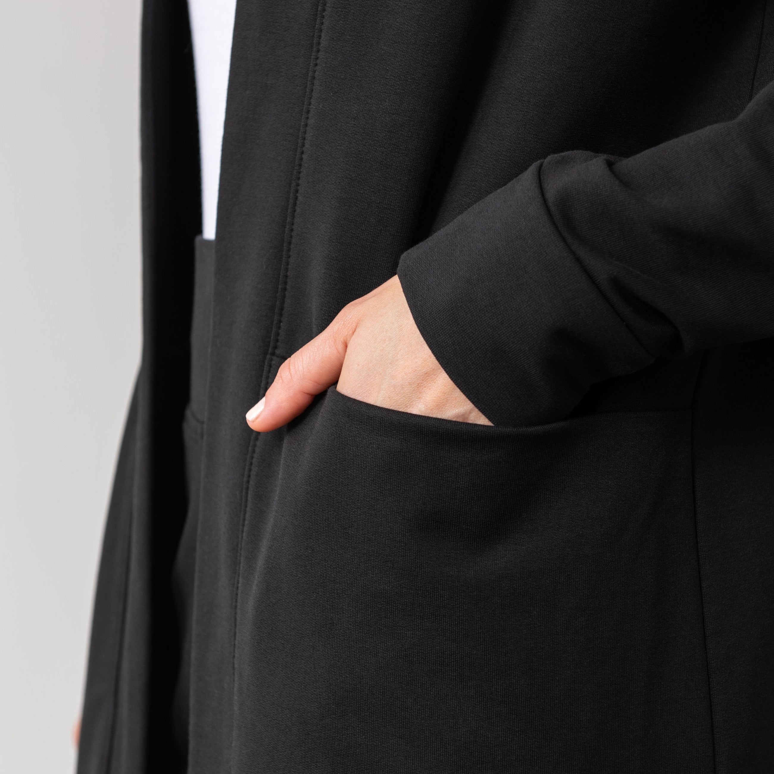 Woman shown wearing black cardigan with hand in her pocket