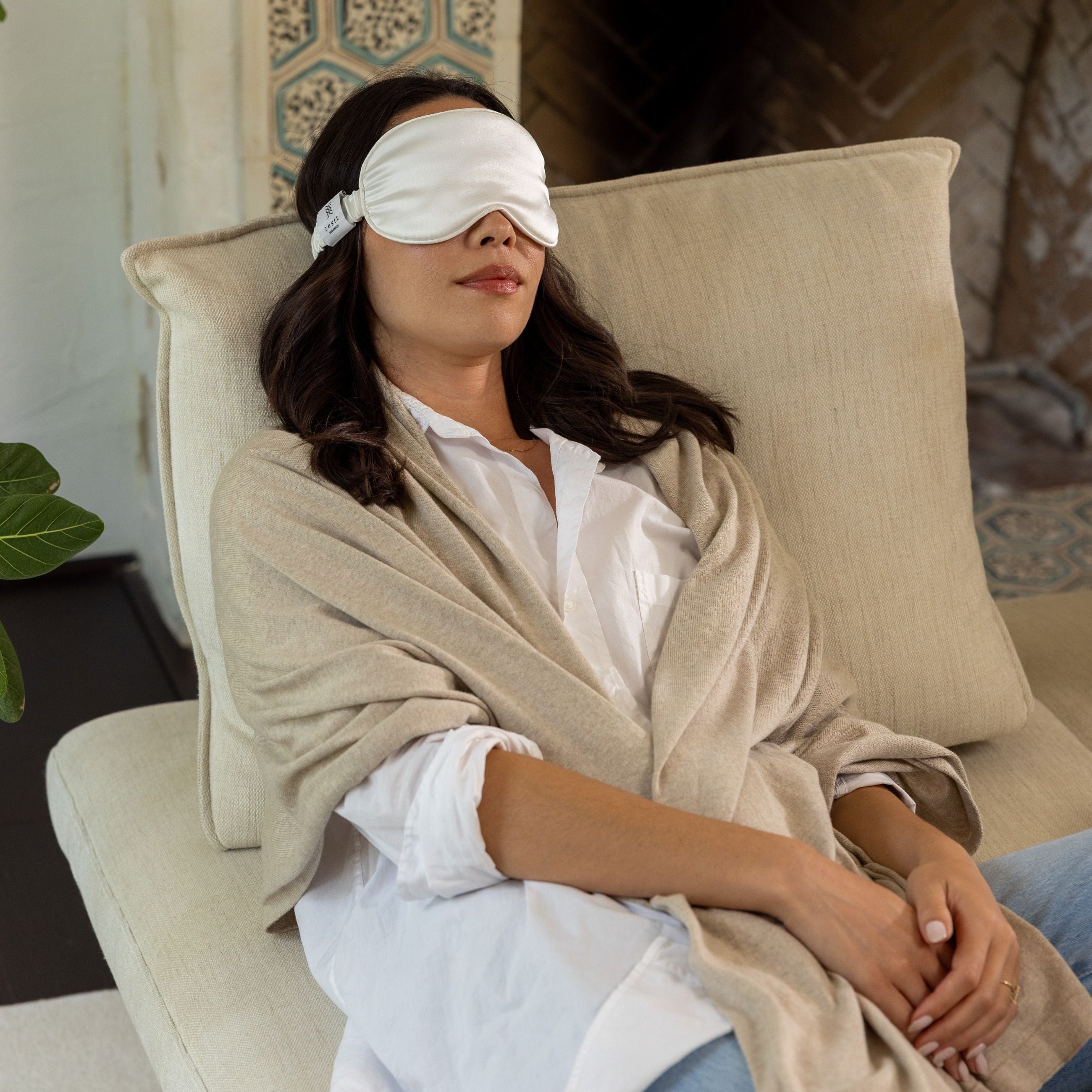 Woman wearing a sleep mask and robe sitting on a couch in a cozy room.
