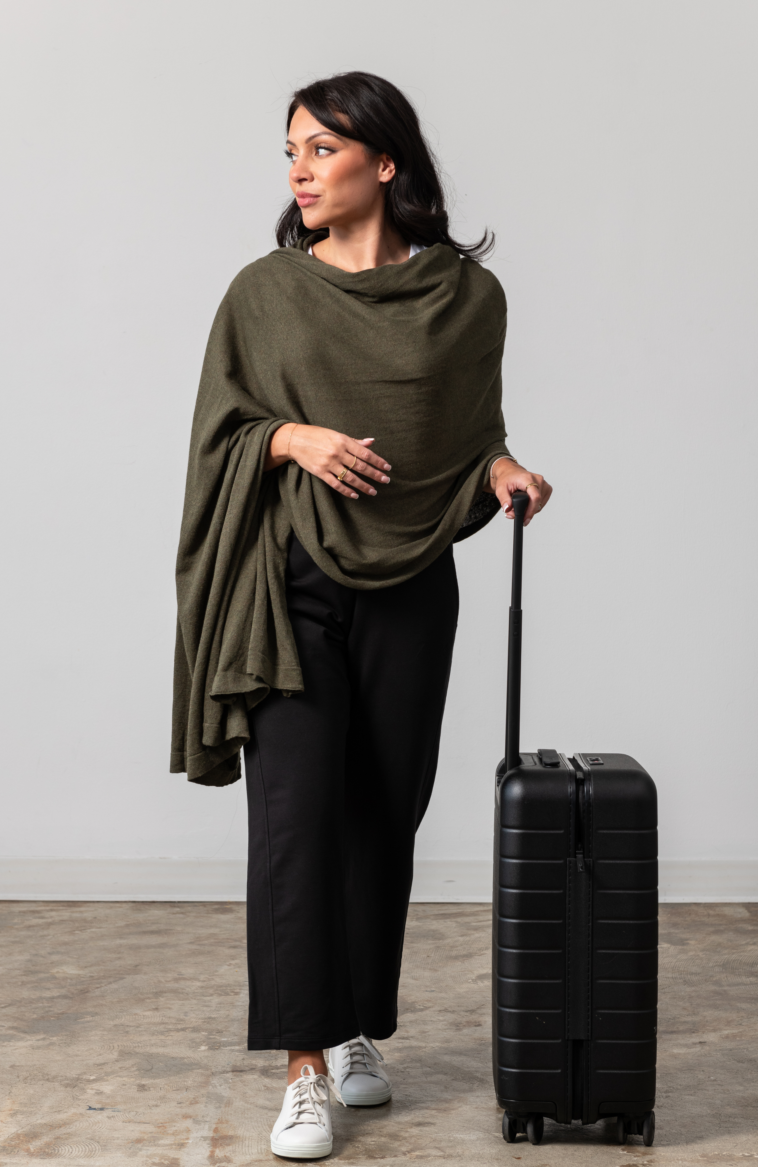Women shown wearing a dark green scarf draped over her shoulders while holding her luggage handle with one hand
