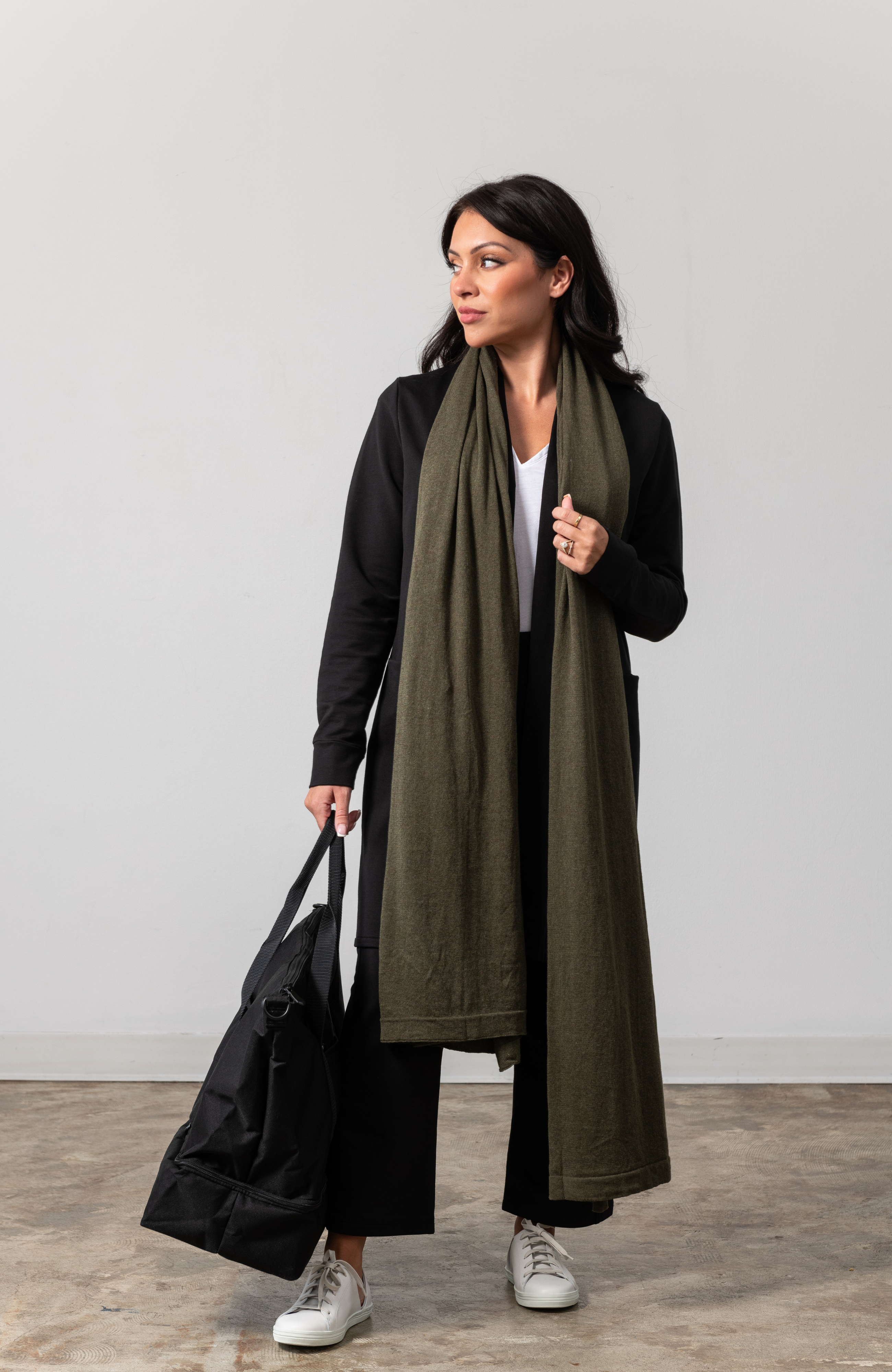 Women shown wearing a dark green scarf draped around her neck while holding her bag with one hand
