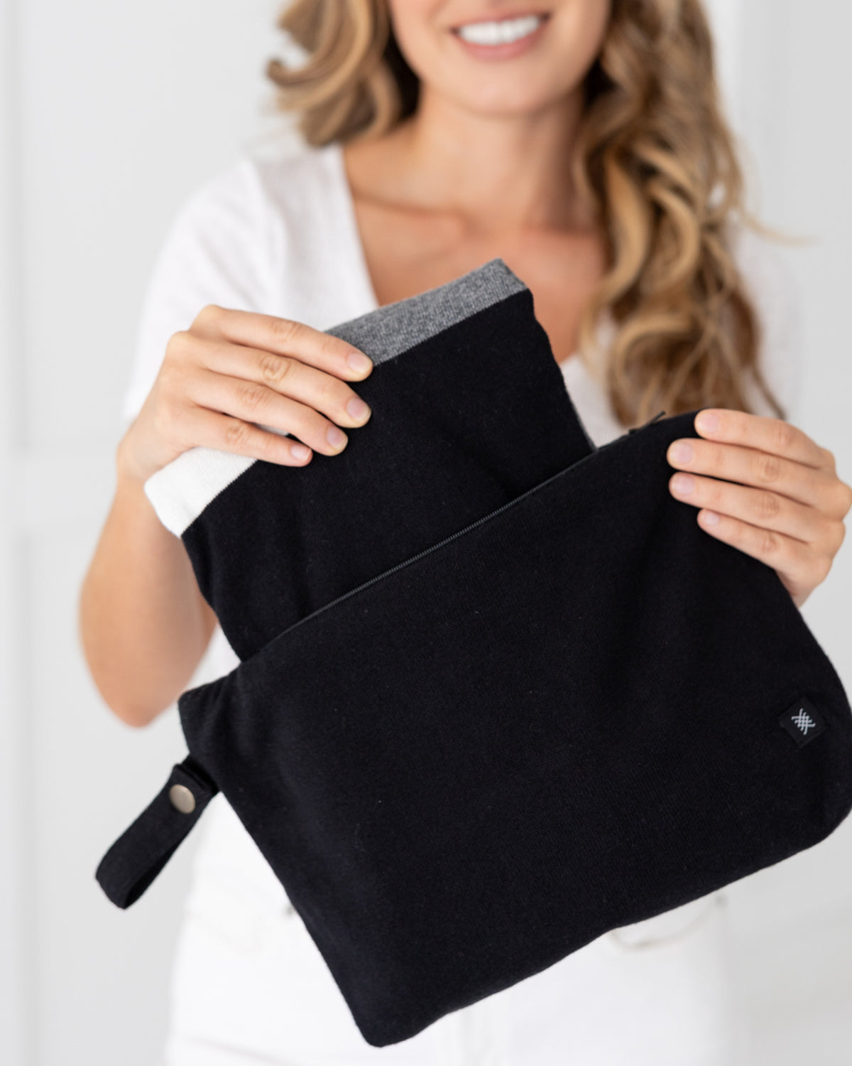 Woman holding Black Carry Pouch,  that can hold the Dreamsoft Travel Scarf, Gray Colorblock Dreamsoft Travel Scarf being shown taken out of the carry pouch.