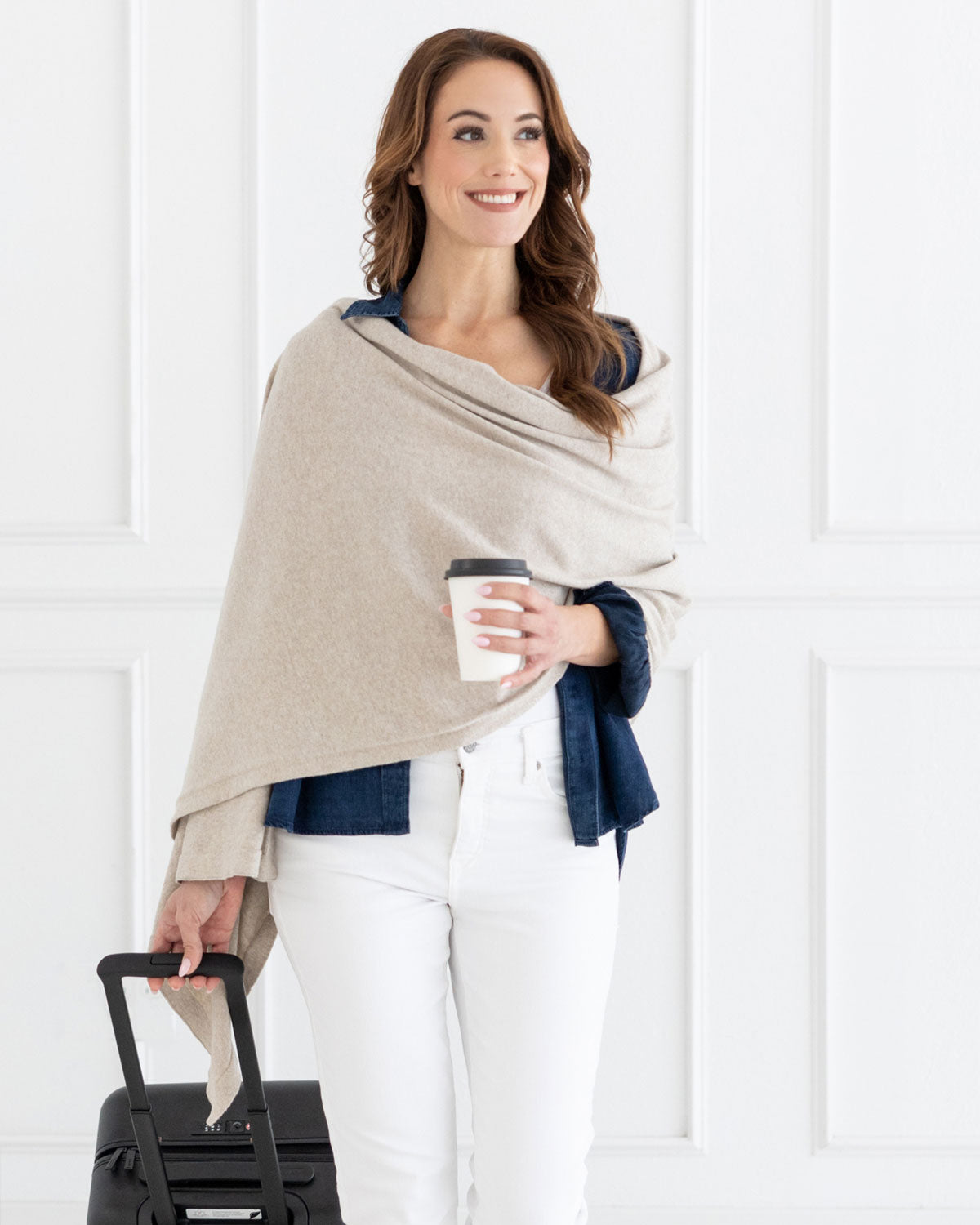 Woman wearing the Dreamsoft Travel Scarf in Birch Scarf which is a cream scarf, pulling a suitcase while holding her coffee cup