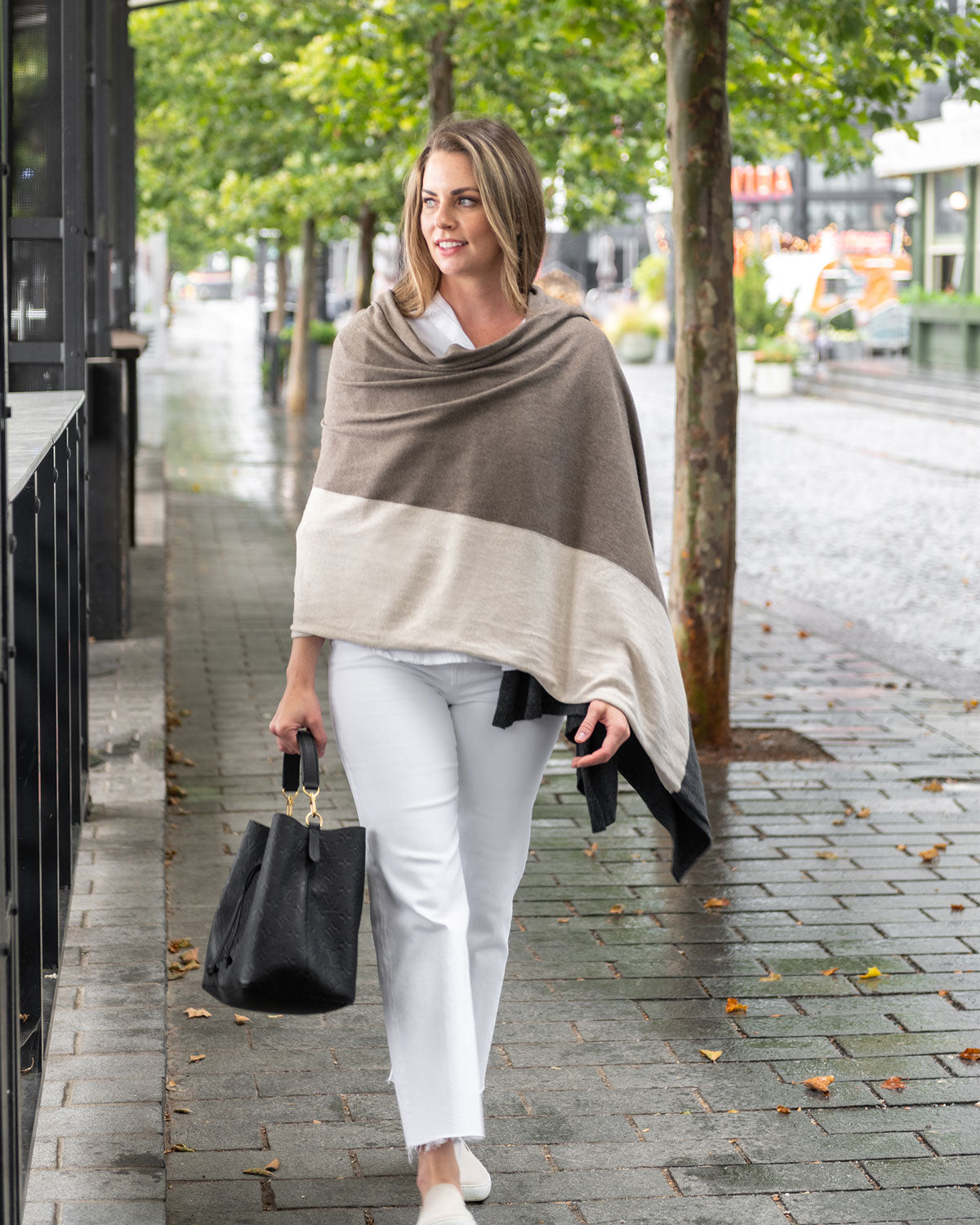 Woman wearing the Dreamsoft Travel Scarf in Brownstone Colorblock which is a brown, tan and gray scarf, walking down the street while carrying her purse