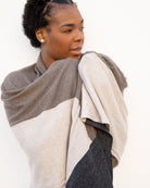 Woman wearing the Dreamsoft Travel Scarf in Brownstone Colorblock which is a brown, tan and gray scarf, worn as the Classic Drape around both of her arms and pulled up to her face