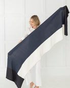 Woman holding the Dreamsoft Travel Scarf in Denim Colorblock which is a dark blue, slate blue and cream scarf