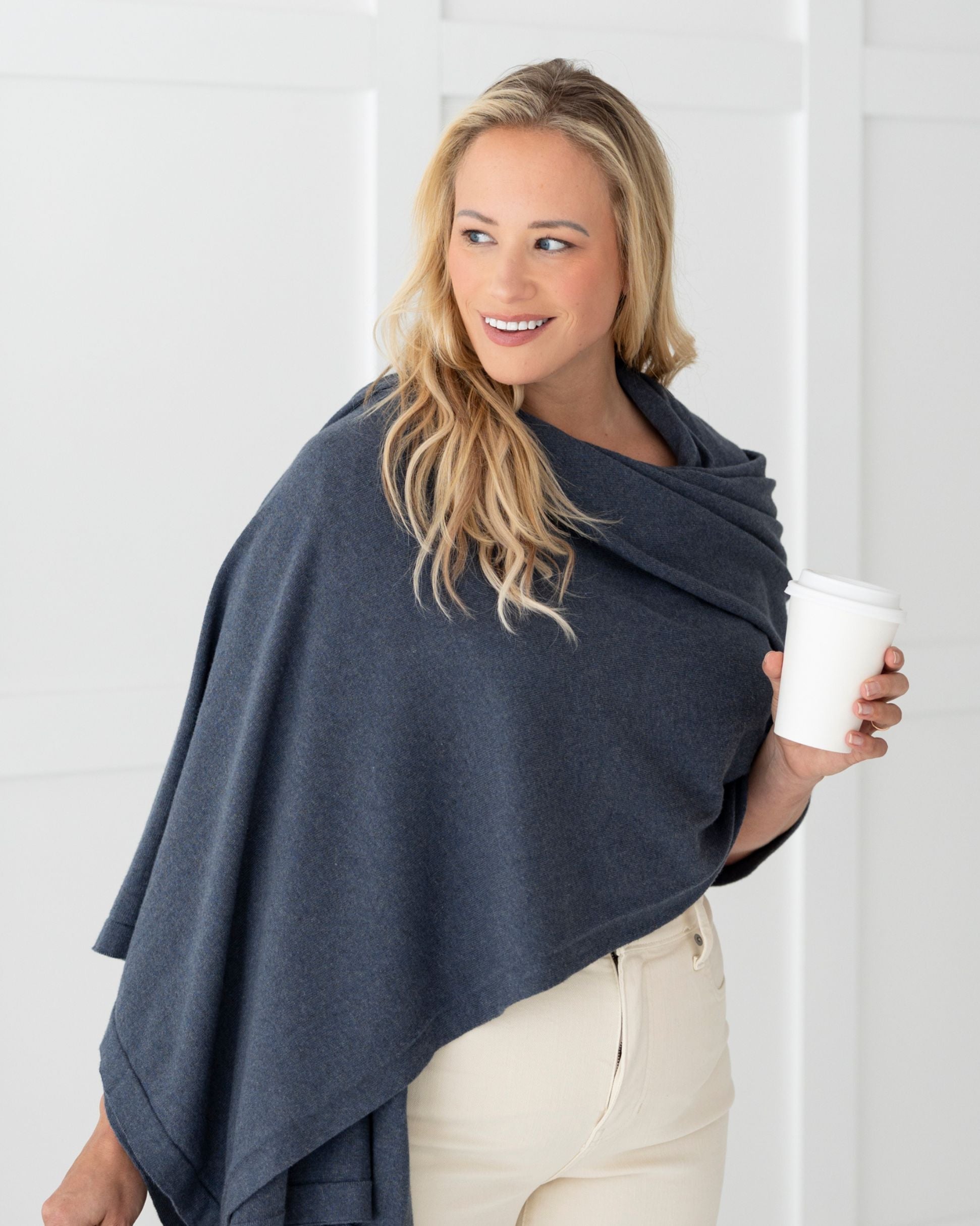 Woman wearing the Denim Dreamsoft Travel Scarf as a wrap, while holding her coffee cup