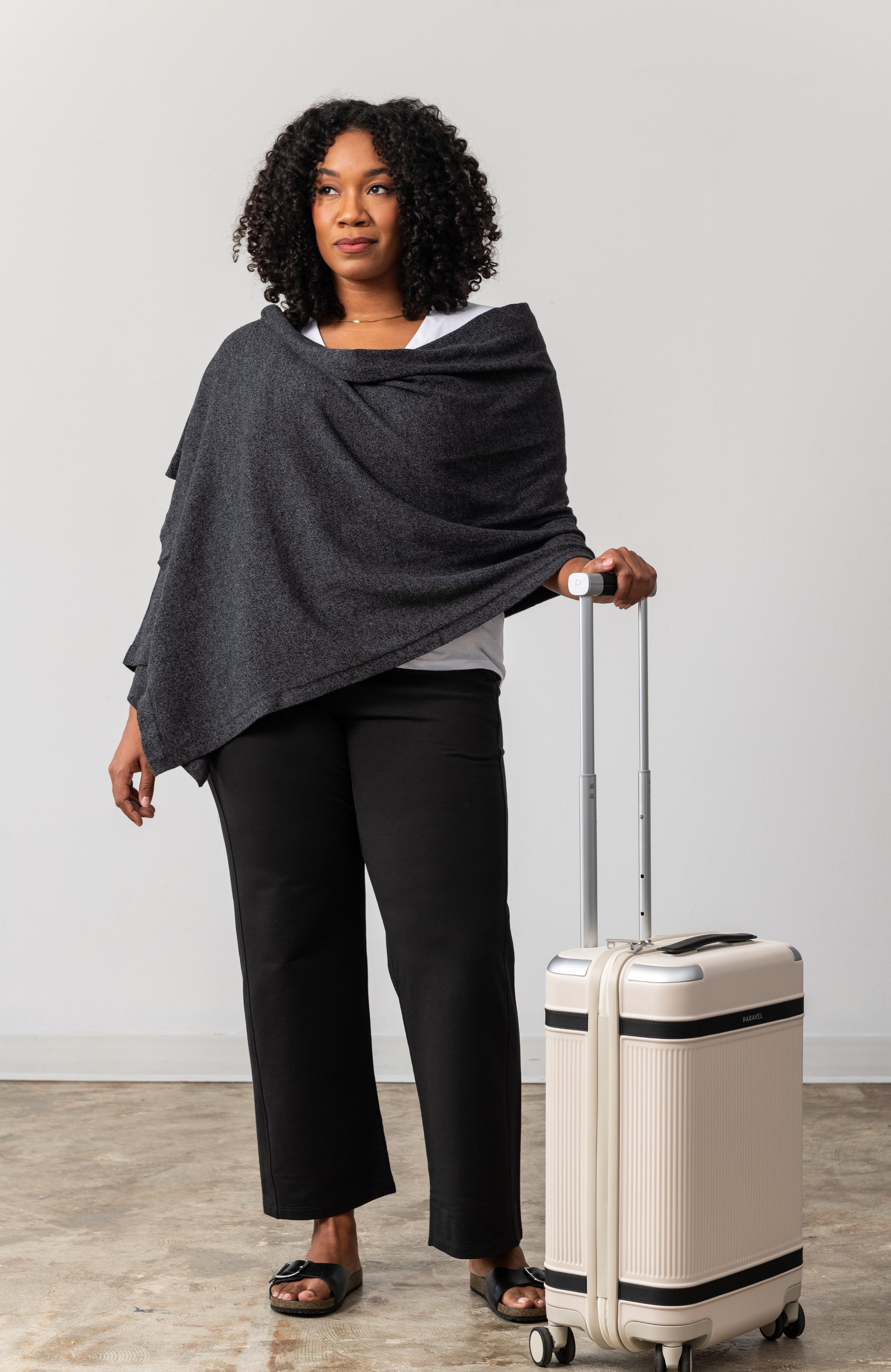 Woman wearing a gray scarf draped around her shoulders with her hand on her luggage handle