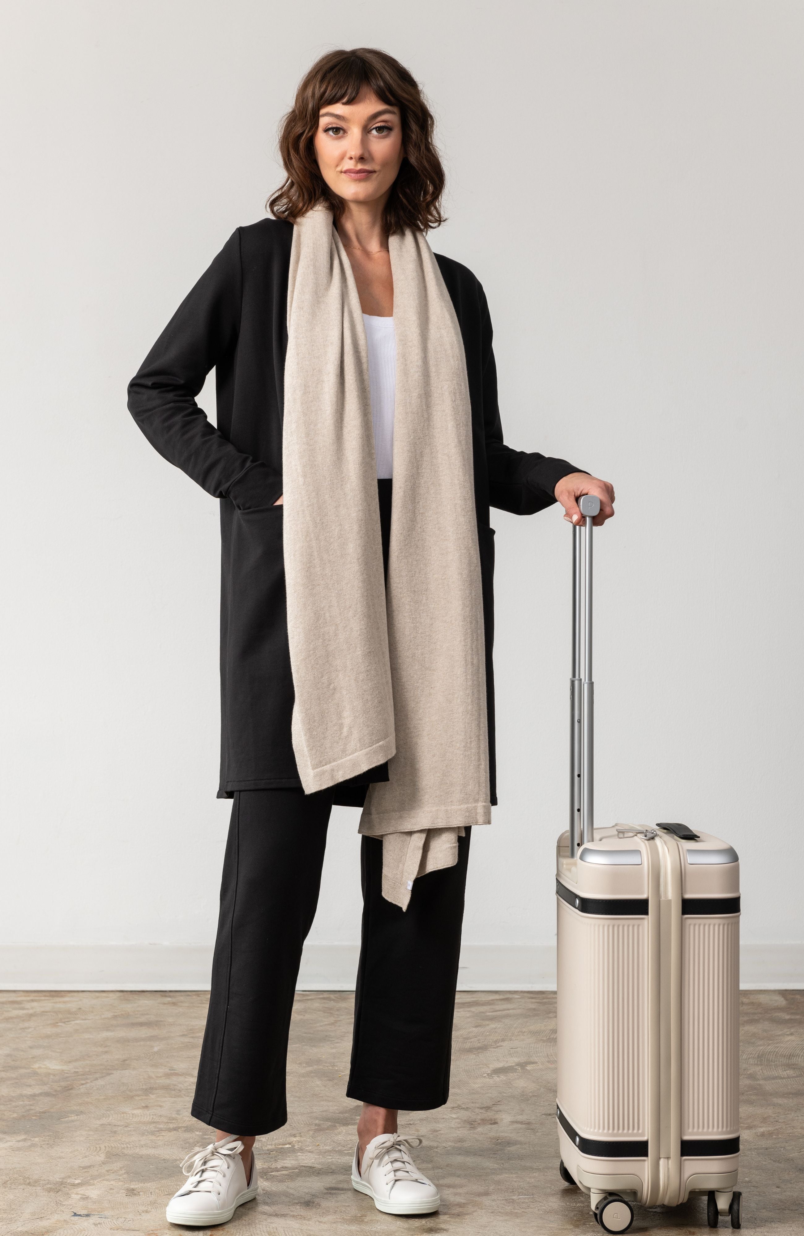 Woman wearing a Beige Scarf draped around her neck and hand on luggage