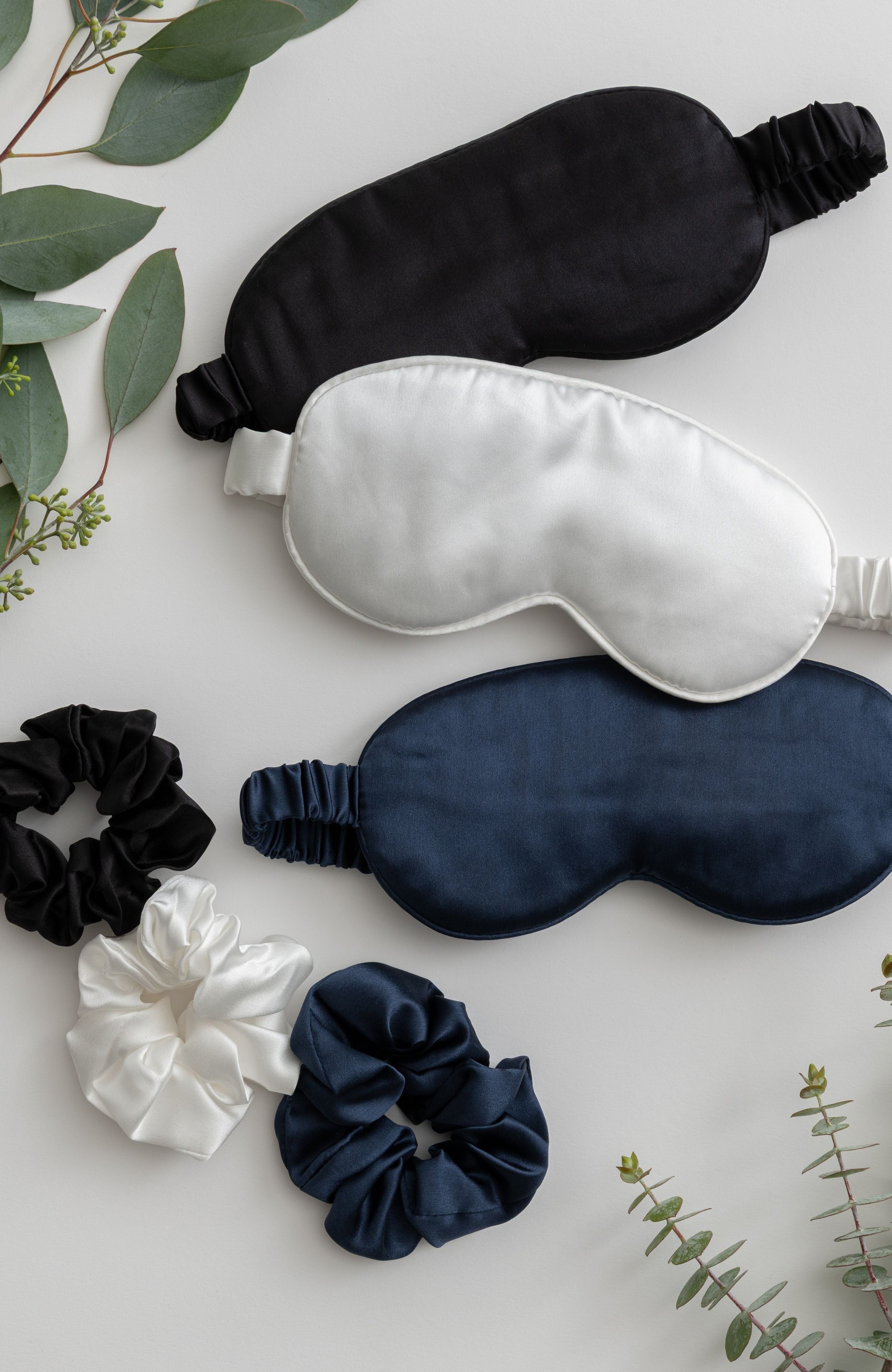 Set of black, white, and navy sleep masks with matching scrunchies on a light background.