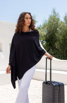 Woman shown wearing Black Scarf wrapped around shoulders with hand on suitcase handle