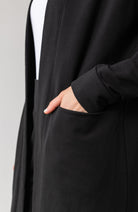 Woman shown wearing black cardigan with hand in her pocket