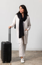 Woman shown wearing Light Beige cardigan with a black scarf around her neck and a hand on her luggage