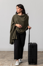 Women shown wearing a dark green scarf draped over her shoulders while holding her  luggage handle with one hand