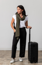 Women shown wearing a dark green scarf wrapped around her neck while holding her  luggage handle with one hand