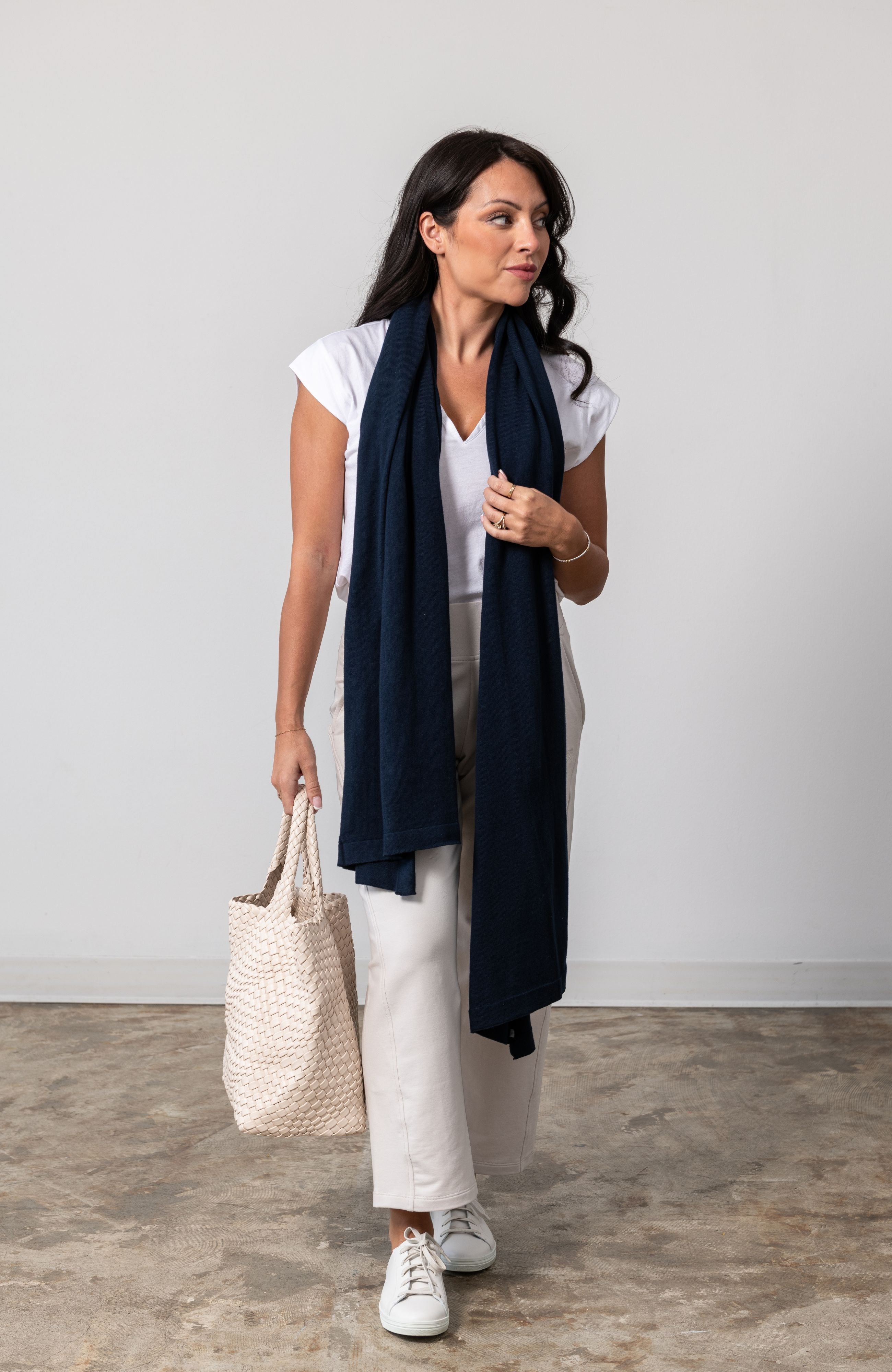 Women shown wearing a dark blue scarf wrapped around her neck holding her bag in one hand