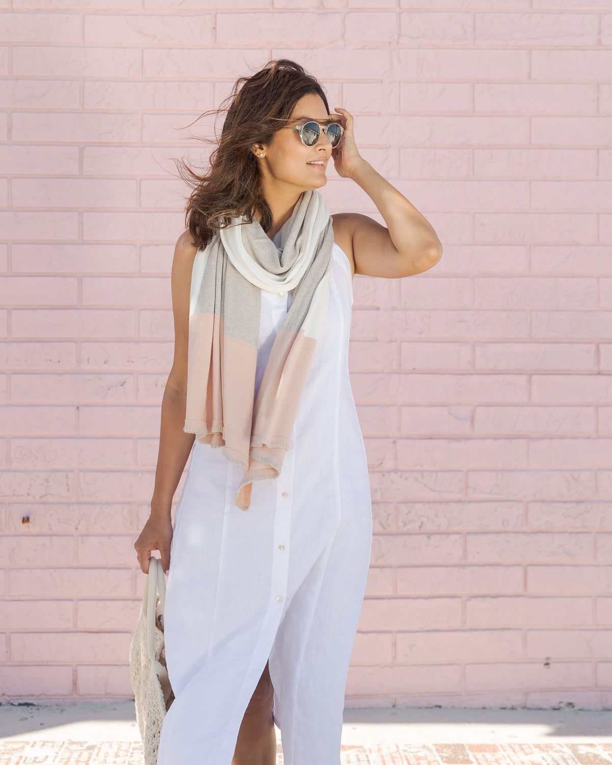 Woman wearing the Dreamsoft Travel Scarf in Blush Colorblock which is a pink, tan and cream scarf,  holding a purse wearing sunglasses with wind blowing her hair