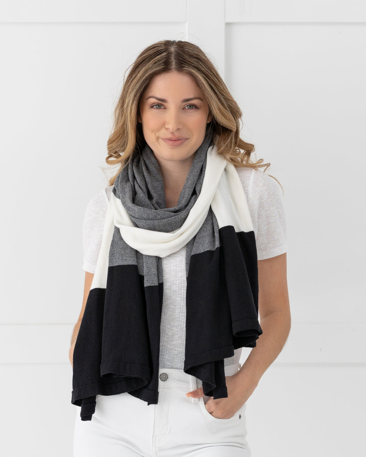 Woman wearing the Dreamsoft Travel Scarf in Gray Colorblock which is a black, gray and cream scarf, while looking at the camera with hands in her pant pockets
