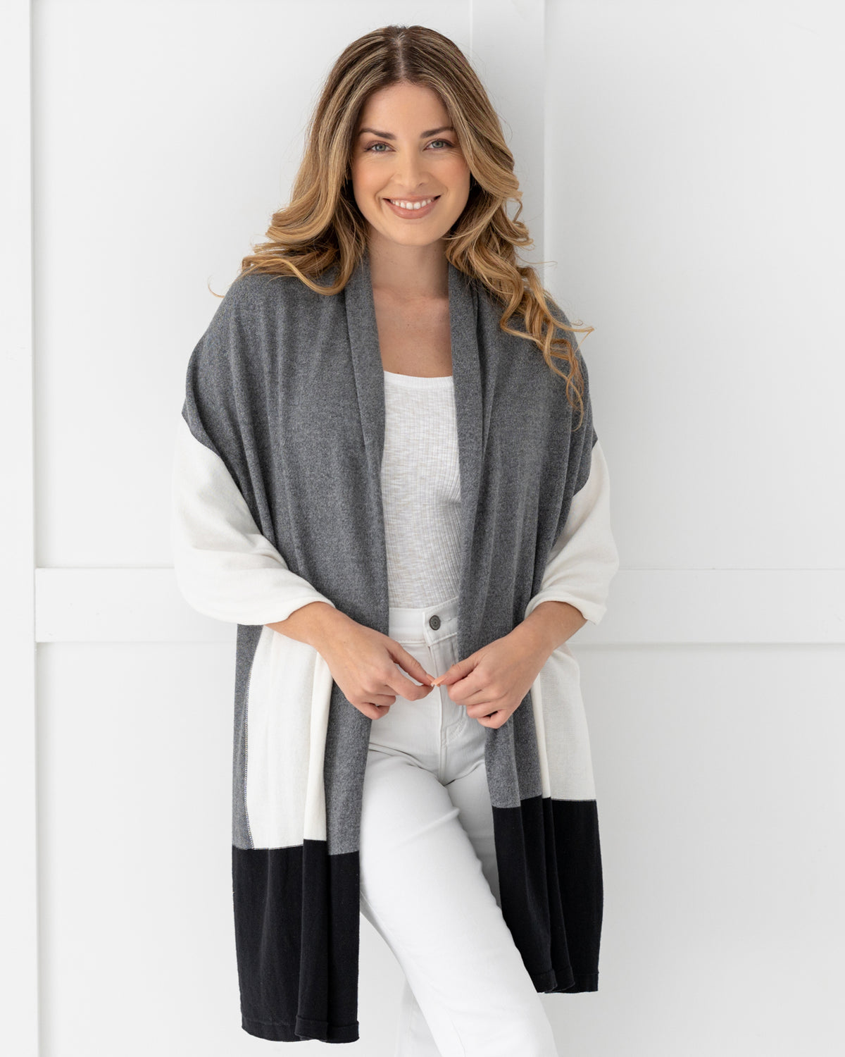 Woman wearing the Dreamsoft Travel Scarf in Gray Colorblock which is a black, gray and cream scarf, wearing as a shawl and smiling at camera