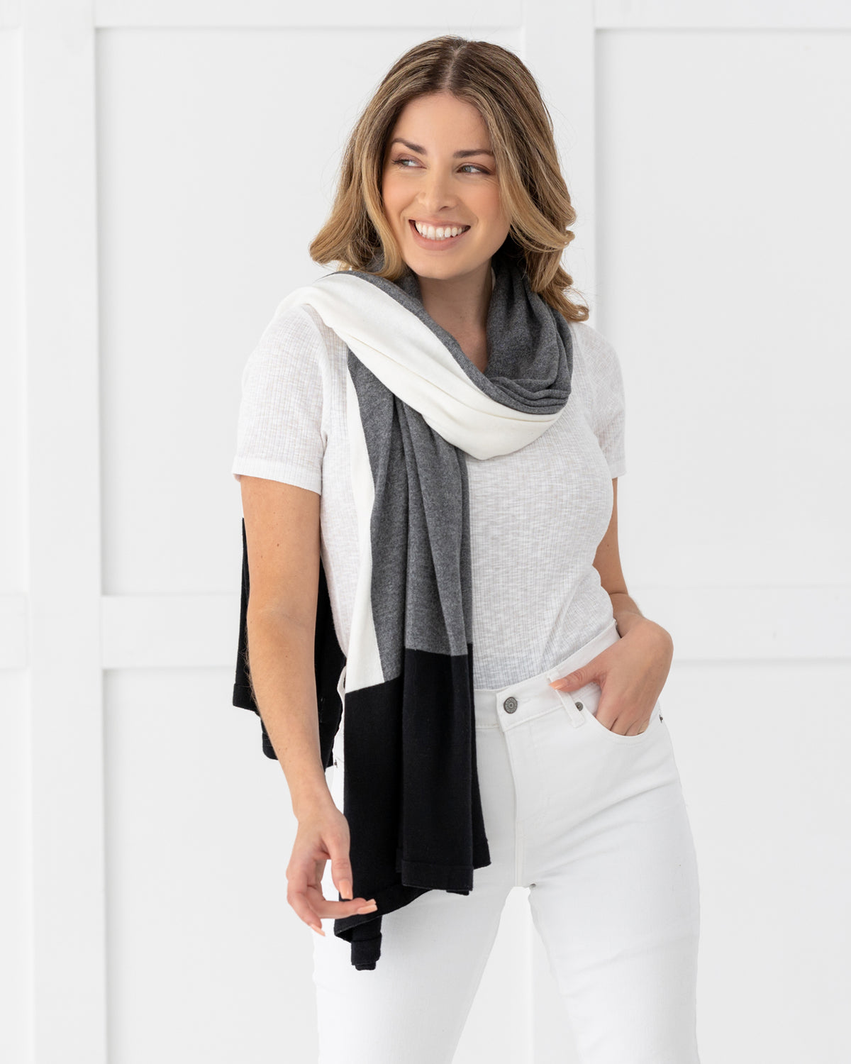 Woman wearing the Dreamsoft Travel Scarf in Gray Colorblock which is a black, gray and cream scarf,  smiling with one hand in her pant pocket