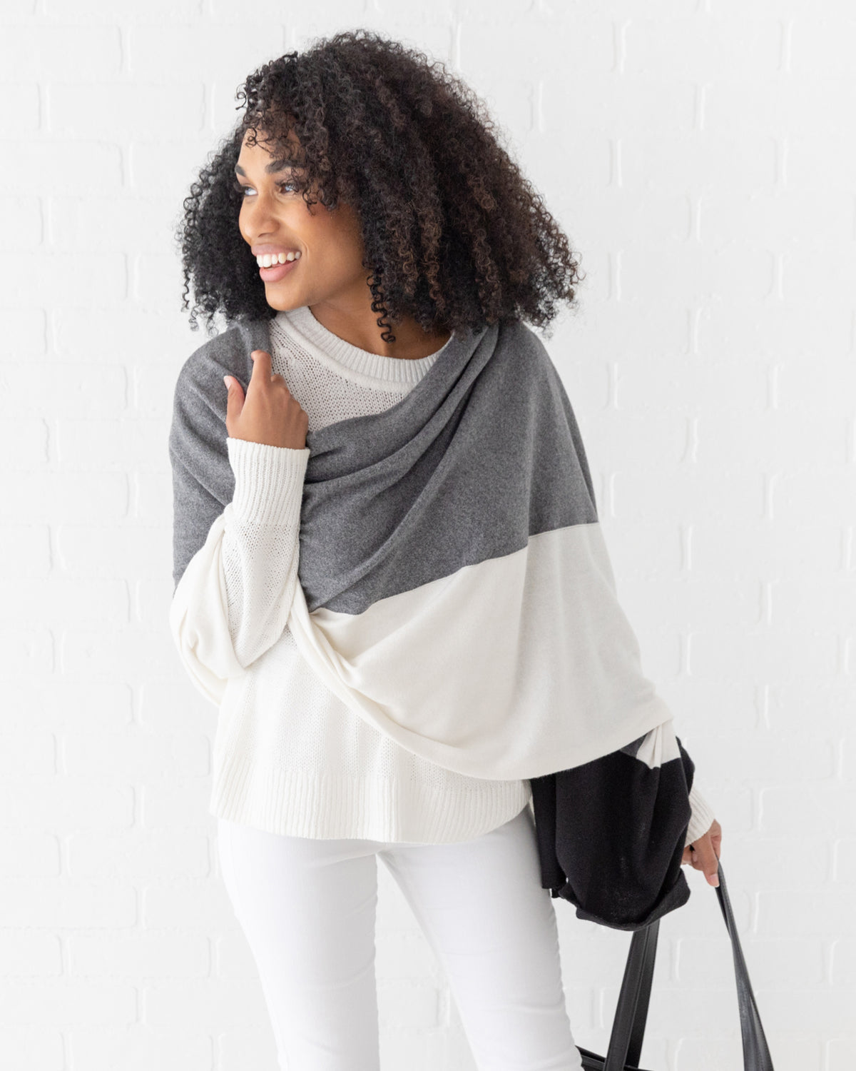Woman wearing the Dreamsoft Travel Scarf in Gray Colorblock which is a black, gray and cream scarf, holding a bag and smiling