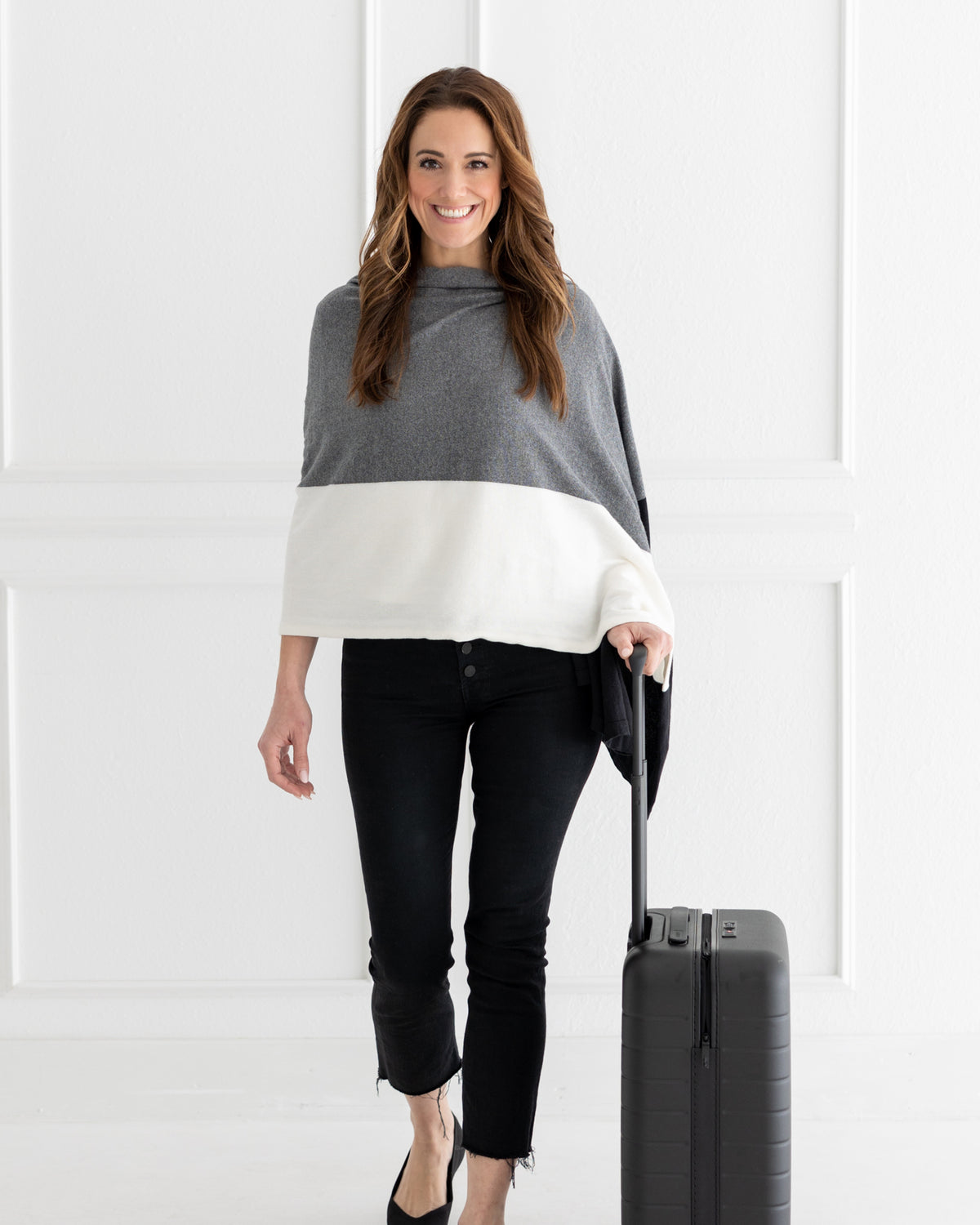 Woman wearing the Dreamsoft Travel Scarf in Gray Colorblock which is a black, gray and cream scarf, hand on a suitcase while smiling